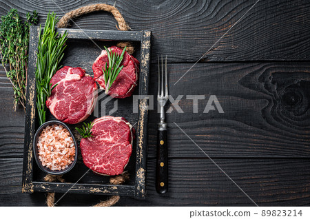 Fillet Mignon tenderloin raw meat veak steaks in wooden tray with herbs. Black wooden background. Top view. Copy space Fillet Mignon tenderloin raw meat veak steaks in wooden tray with herbs. Black wooden background. Top view. Copy space 89823214