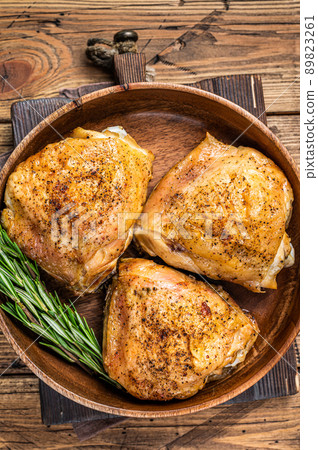 Roasted chicken thighs in a wooden plate with rosemary and herbs. wooden background. Top View 89823261