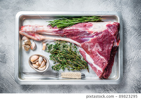 Uncooked Raw goat or lamb leg with herbs in baking tray. White background. Top view 89823295