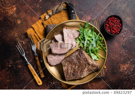 Roast Tri Tip or sirloin bottom beef steak on a plate with arugula. Dark background. Top view Roast Tri Tip or sirloin bottom beef steak on a plate with arugula. Dark background. Top view 89823297