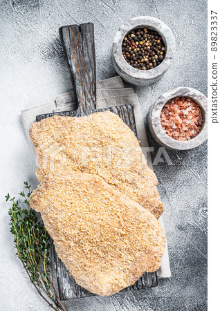 Wiener Raw schnitzel in breadcrumbs on wooden board. White background. Top view Wiener Raw schnitzel in breadcrumbs on wooden board. White background. Top view 89823337