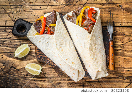 Fajitas Tortilla wrap with beef meat stripes, colored bell pepper and onions and salsa. Wooden background. Top view 89823398