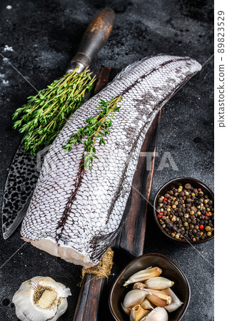 Raw grenadier macrurus white fish on a wooden cutting board. Black background. Top view 89823529