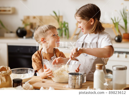 Happy children brother and sister making dough and cooking together in kitchen Happy children brother and sister making dough and cooking together in kitchen 89823612