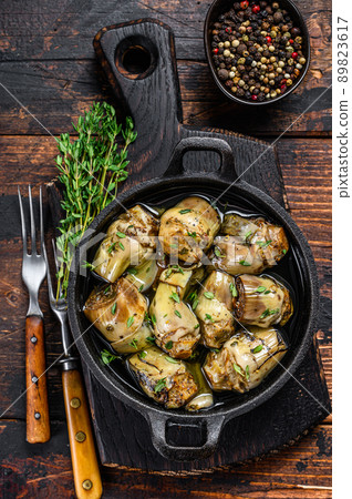Marinated artichokes in olive oil in a pan. Dark wooden background. Top view 89823617