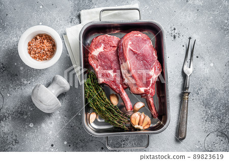 Uncooked Raw Tomahawk veal steaks in steel tray with herbs. Gray background. Top view 89823619