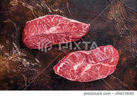 Raw Top Blade or flat iron beef meat steaks on a butcher table. Dark background. Top View Raw Top Blade or flat iron beef meat steaks on a butcher table. Dark background. Top View 89823689