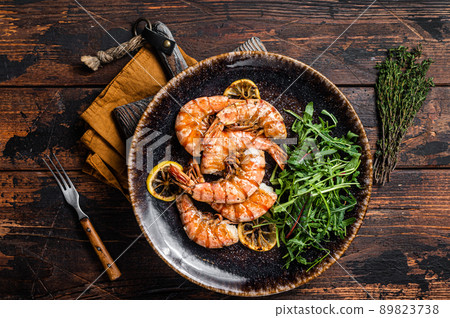 Spicy garlic Giant shrimps prawns in plate with salad. Wooden background. Top view Spicy garlic Giant shrimps prawns in plate with salad. Wooden background. Top view 89823738
