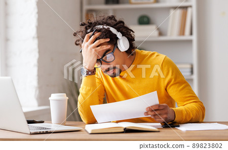 Frustrated young african american in glasses and headphones suffering from headache feeling stressed with work at laptop 89823802