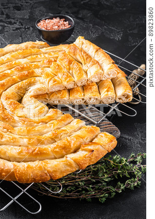 Turkish Tepsi Boregi, Round Borek cheese pie on kitchen board. Black background. Top view 89823860