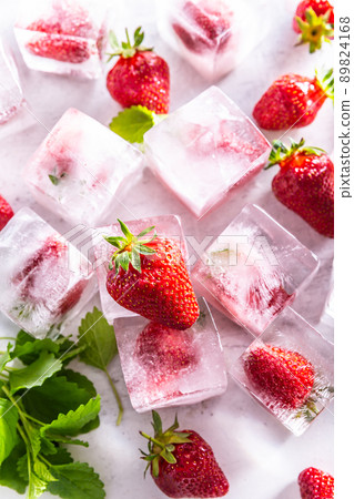 Strawberries frozen in ice cubes with mellisa leaves - Top of view. Strawberries frozen in ice cubes with mellisa leaves - Top of view. 89824168