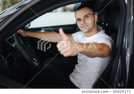 Handseome man in white t-shirt sitting in his new car in car showroom. Male give his thumb up Handseome man in white t-shirt sitting in his new car in car showroom. Male give his thumb up 89824171