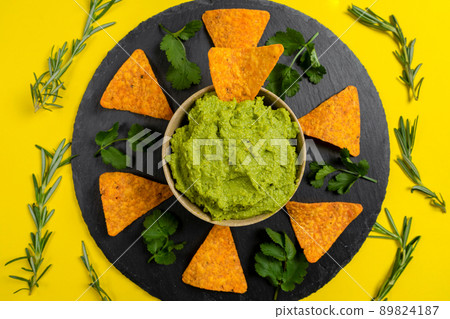 Composition of guacamole with aromatic herbs for decoration and nachos for consumption on a yellow background. Composition of guacamole with aromatic herbs for decoration and nachos for consumption on a yellow background. 89824187