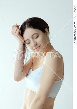 Portrait of tender young woman posing in white underwear, with eyes closed isolated over grey studio background 89825552