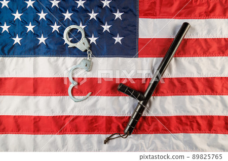 silver metal handcuffs and police nightstick over US flag on flat surface silver metal handcuffs and police nightstick over US flag on flat surface 89825765