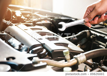 Auto mechanic hand holding open-end spanner on the engine compartment in the auto repair garage 89826881
