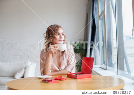 Attractive lady sitting at the table, drinking coffee or tea and eating chocolate at home 89828237