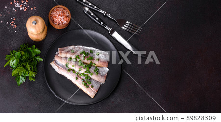 Delicious fresh herring fillet with salt, spices and herbs on a black plate Delicious fresh herring fillet with salt, spices and herbs on a black plate 89828309