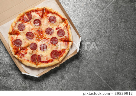 Hot delicious pepperoni pizza in cardboard box on grey table, top view. Space for text 89829912