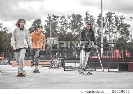 Girl and two guys riding skateboards in park 89829951