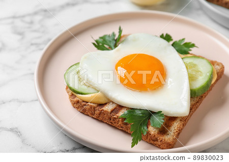 Plate of tasty sandwich with heart shaped fried egg on white marble table, closeup 89830023
