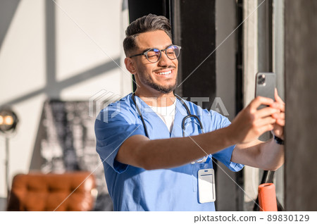 Physician with a radiant smile taking photos of himself 89830129