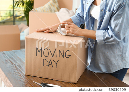 Woman packing box with words MOVING DAY at wooden table, closeup 89830309