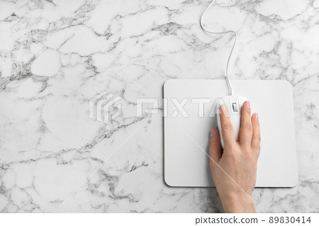 Woman using modern wired optical mouse on white marble table, top view. Space for text 89830414