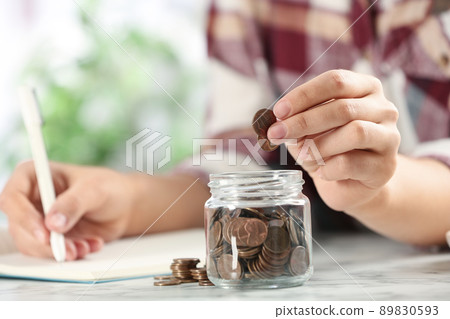Woman putting money into glass jar at white marble table, closeup 89830593