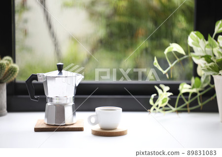 White coffee cup and stainless moka pot in front of window White coffee cup and stainless moka pot in front of window 89831083