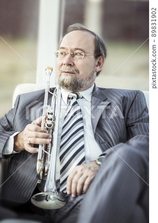 portrait of a musician with a trumpet sitting in a chair, on the background of the concert hall portrait of a musician with a trumpet sitting in a chair, on the background of the concert hall 89831902