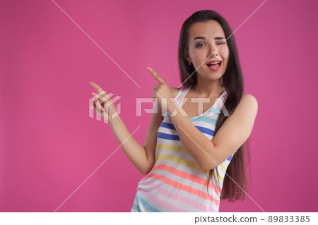 Brunette woman with long hair, dressed in colorful striped shirt, posing against pink studio background. Sincere emotions. Close-up. Brunette woman with long hair, dressed in colorful striped shirt, posing against pink studio background. Sincere emotions. Close-up. 89833385