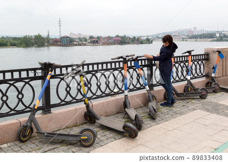 A woman cautiously inspects the rental of electric scooters A woman cautiously inspects the rental of electric scooters 89833408