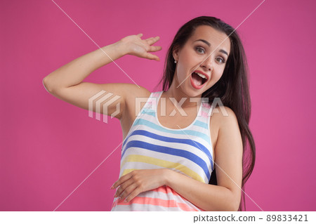 Brunette woman with long hair, dressed in colorful striped shirt, posing against pink studio background. Sincere emotions. Close-up. Brunette woman with long hair, dressed in colorful striped shirt, posing against pink studio background. Sincere emotions. Close-up. 89833421