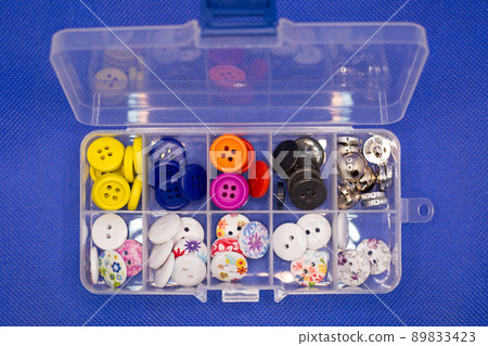 Small buttons for clothes of different types lie in the cells of a plastic container 89833423
