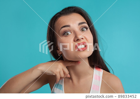 Brunette woman with long hair, dressed in colorful striped shirt, posing against blue studio background. Sincere emotions. Close-up. Brunette woman with long hair, dressed in colorful striped shirt, posing against blue studio background. Sincere emotions. Close-up. 89833452