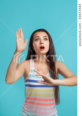 Brunette woman with long hair, dressed in colorful striped shirt, posing against blue studio background. Sincere emotions. Close-up. 89833484