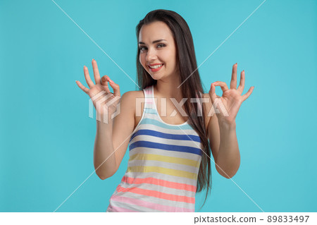 Brunette woman with long hair, dressed in colorful striped shirt, posing against blue studio background. Sincere emotions. Close-up. 89833497