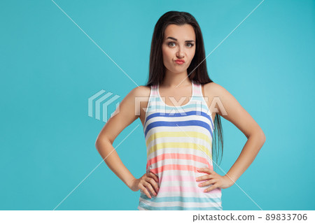 Brunette woman with long hair, dressed in colorful striped shirt, posing against blue studio background. Sincere emotions. Close-up. Brunette woman with long hair, dressed in colorful striped shirt, posing against blue studio background. Sincere emotions. Close-up. 89833706