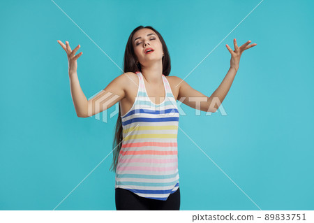 Brunette woman with long hair, dressed in striped shirt and black leggings, posing against blue studio background. Sincere emotions. Close-up. Brunette woman with long hair, dressed in striped shirt and black leggings, posing against blue studio background. Sincere emotions. Close-up. 89833751