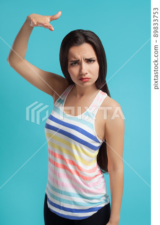 Brunette woman with long hair, dressed in striped shirt and black leggings, posing against blue studio background. Sincere emotions. Close-up. 89833753