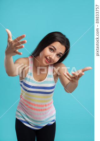 Brunette woman with long hair, dressed in striped shirt and black leggings, posing against blue studio background. Sincere emotions. Close-up. Brunette woman with long hair, dressed in striped shirt and black leggings, posing against blue studio background. Sincere emotions. Close-up. 89833757