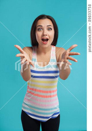 Brunette woman with long hair, dressed in striped shirt and black leggings, posing against blue studio background. Sincere emotions. Close-up. Brunette woman with long hair, dressed in striped shirt and black leggings, posing against blue studio background. Sincere emotions. Close-up. 89833758