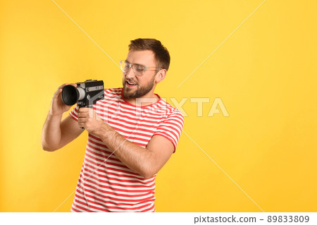 Young man with vintage video camera on yellow background, space for text Young man with vintage video camera on yellow background, space for text 89833809