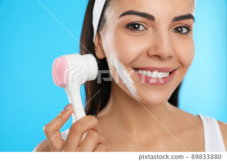Young woman using facial cleansing brush on light blue background, closeup. Washing accessory Young woman using facial cleansing brush on light blue background, closeup. Washing accessory 89833880