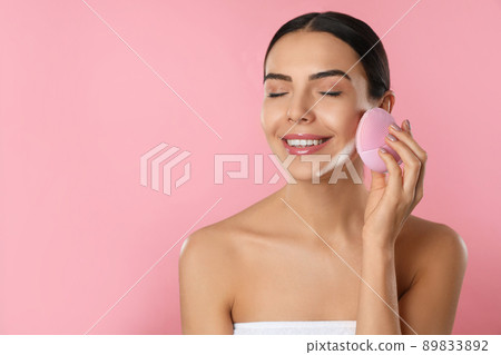 Young woman using facial cleansing brush on pink background, space for text. Washing accessory 89833892