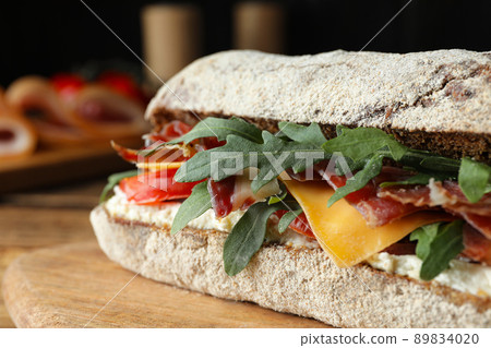 Delicious sandwich with fresh vegetables and prosciutto on wooden table, closeup 89834020