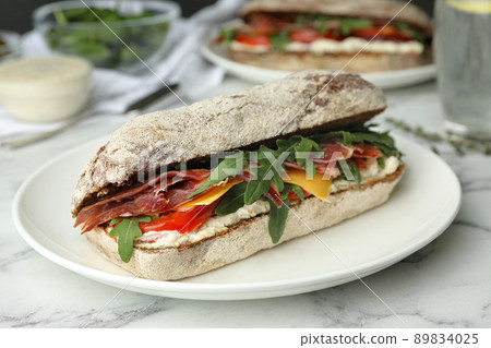 Delicious sandwich with fresh vegetables and prosciutto on white marble table 89834025