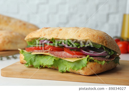 Delicious sandwich with fresh vegetables and salami on white table 89834027