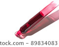 Liquid red oil serum drop in pipette isolated on white background. Retinol, aha acid, collagen skincare fluid, close up photo with shallow depth of field. Transparent crimson essence in dropper 89834083
